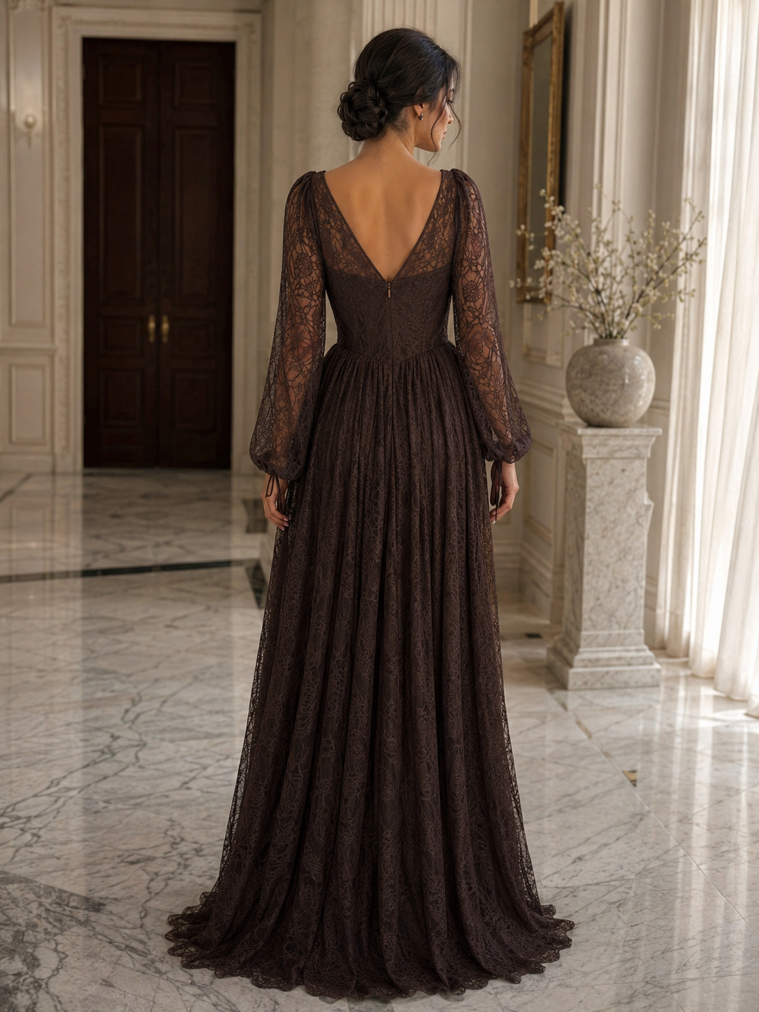 A woman wearing a floor-length dark brown lace gown, shown from the back in an elegant indoor hallway with marble floors and a stone pillar.

