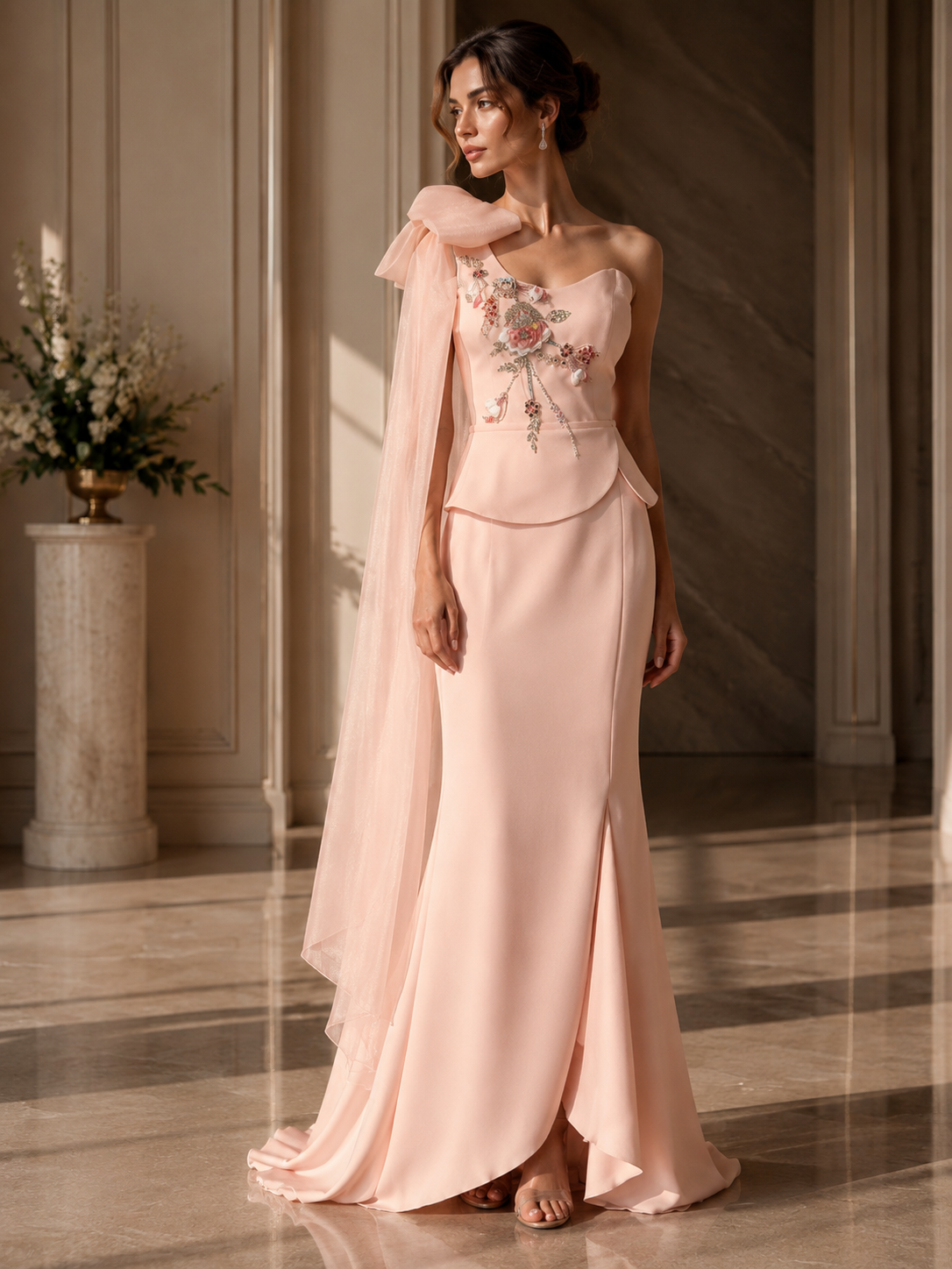 Woman in a pink evening gown with floral embroidery in an elegant indoor setting.

