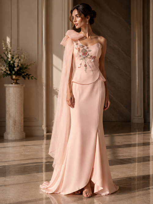 Woman in a pink evening gown with floral embroidery in an elegant indoor setting.

