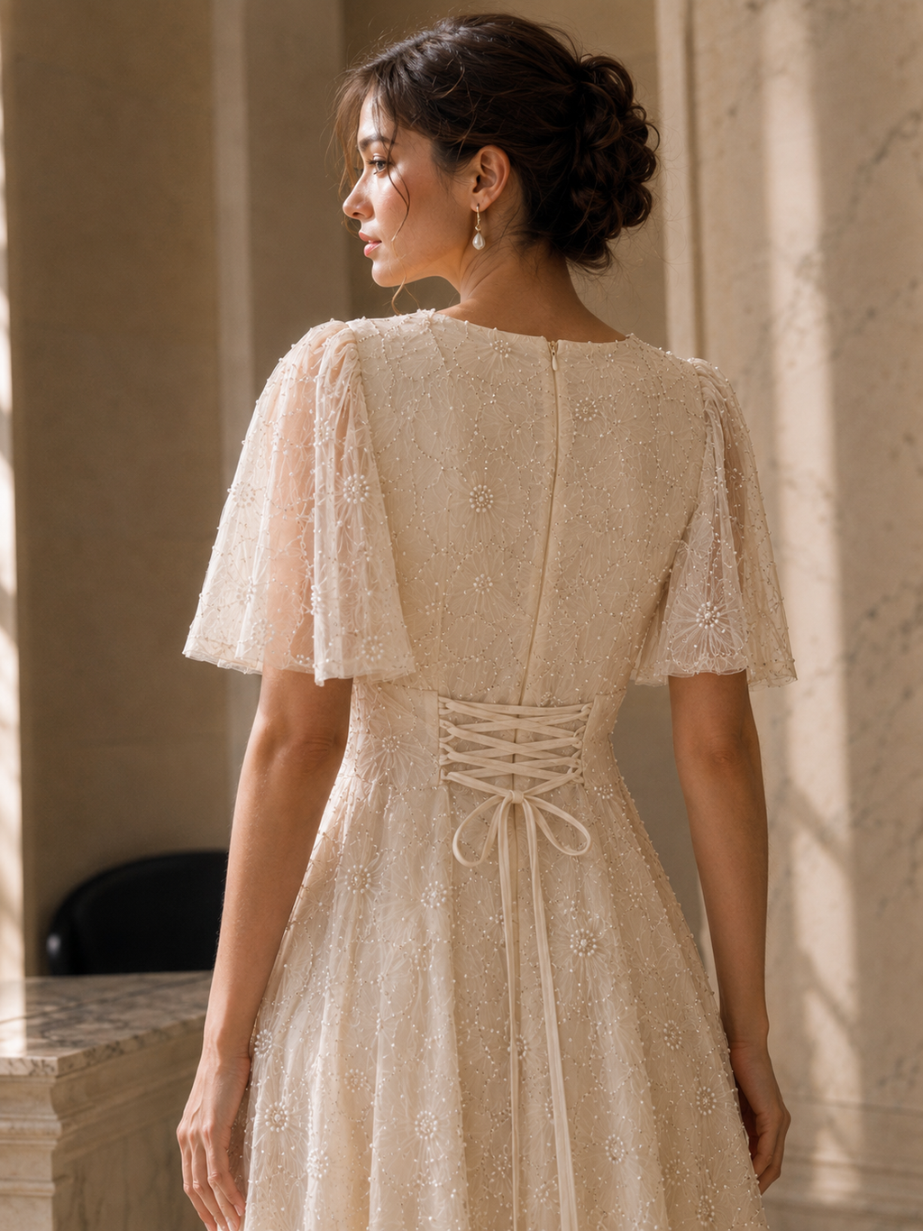 Close-up back view of ivory embroidered dress showing sheer sleeves, zipper, floral beadwork, and lace-up waist
